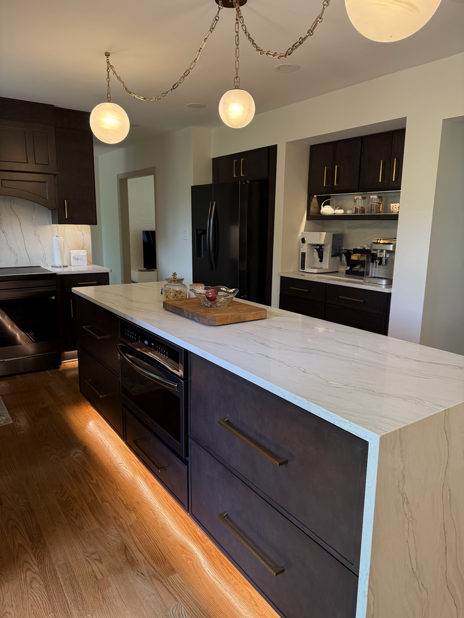 Open-Concept Kitchen — Wall removed to open the space, marble waterfall counters, and globe pendants.